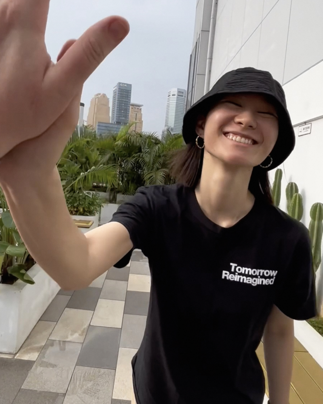 Un membre de l&#039;équipe ZURU se tient à l&#039;extérieur et sourit à la caméra. Il porte un chapeau noir et un t-shirt noir &quot;Tomorrow Reimagined&quot; (Demain réinventé).